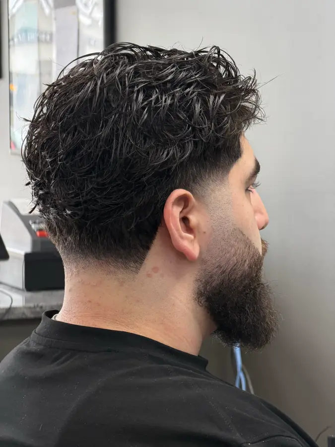 Textured curly top over a low fade, with a full beard